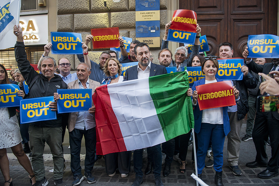 Лидер партии «Лига Севера» Маттео Сальвини (в центре) держит итальянский флаг, а его сторонники держат плакаты с надписью «Урсула, вон, позор вам» во время акции протеста перед офисом Европейской комиссии.