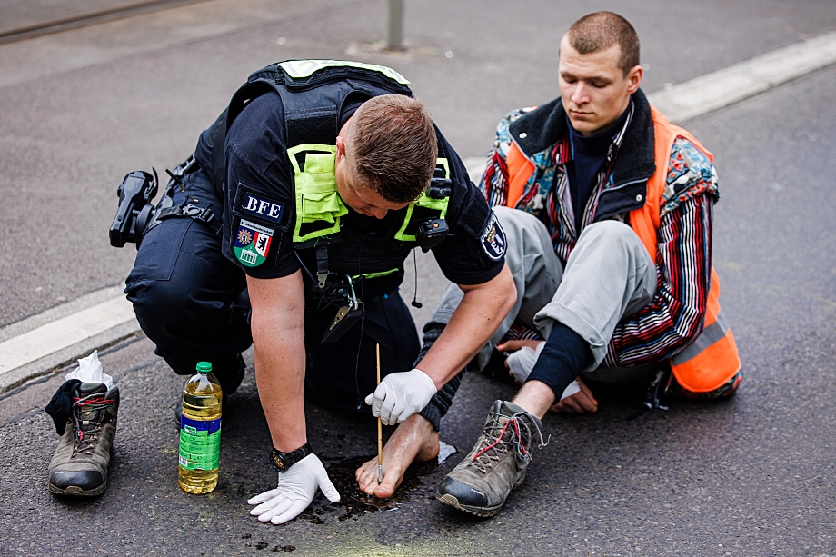 Полицейский в Берлине пытается отклеить от асфальта ногу активиста из «Последнего поколения».