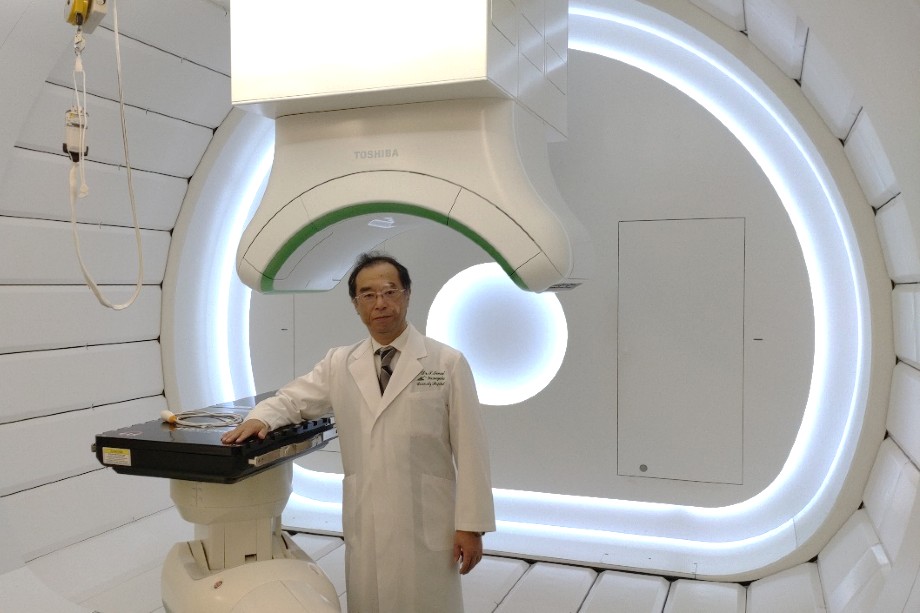 Директор Центра терапии тяжёлыми ионами при медицинском факультете Университета Ямагата Иваи Такэо рядом с установкой для облучения тяжёлыми ионами.